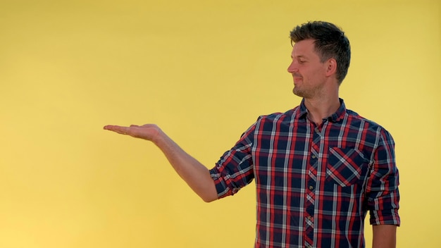 Handsome man presenting something on empty hand with yellow background he looking on copy space for ...