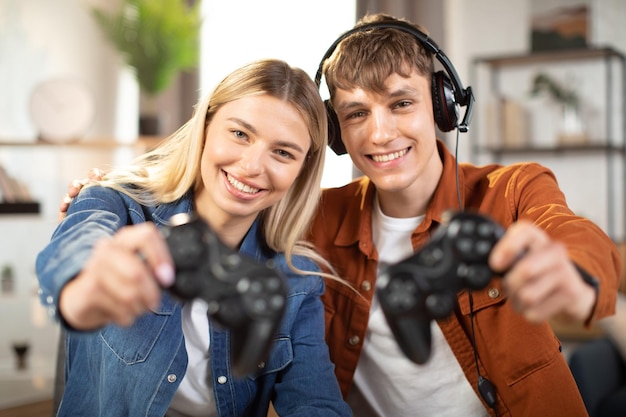 handsome man and pretty blond woman showing wireless joysticks to camera
