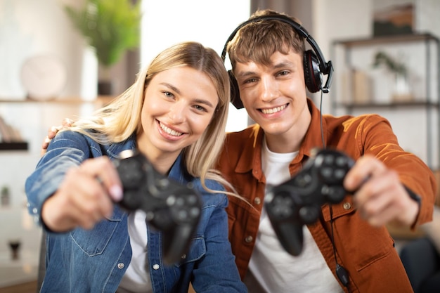 Handsome man and pretty blond woman showing wireless joysticks to camera