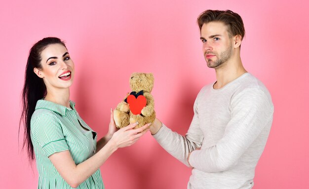 Handsome man and pretty girl in love. Man and woman couple in love hold heart valentines cards and teddy bear on pink background. Romantic couple in love. Valentines day and love. Cute gift concept.
