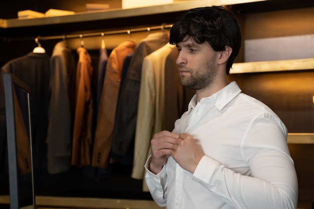 Handsome man puts on a shirt while standing in his dressing room male putting on stylish elegant shirt before meeting