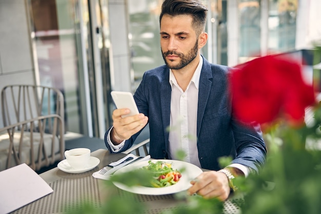 Красивый мужчина читает сообщение перед тем, как съесть салат перед поездкой на конференцию