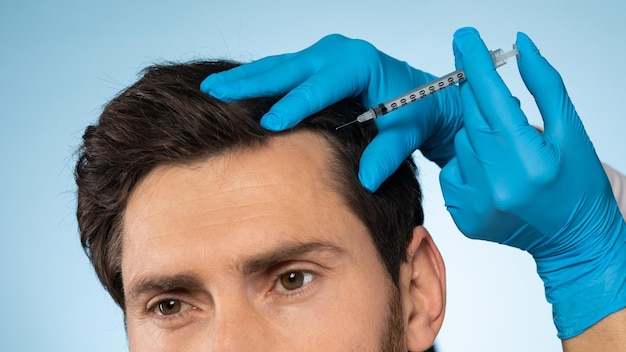 Handsome man receiving injections in his head having mesotherapy session blue background panorama