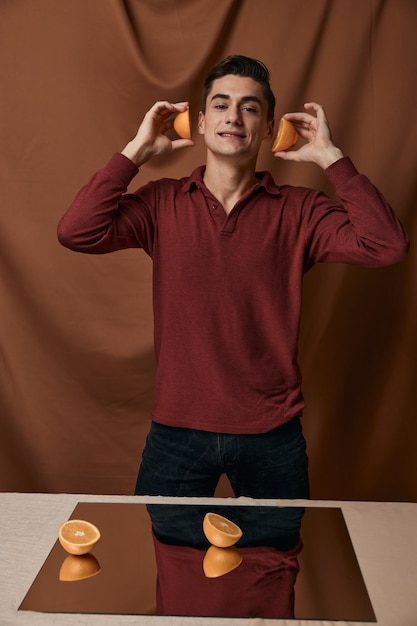 Handsome man in red shirt with oranges near face smile fabric background