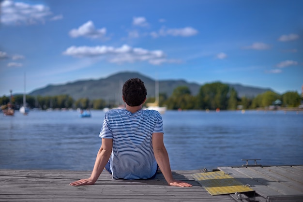 Handsome man relax and sitting on the pier and looking on boats.  Summer vacations