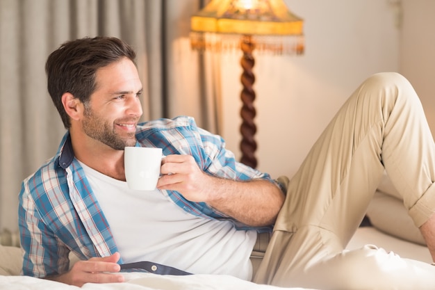 Handsome man relaxing on his bed with hot drink