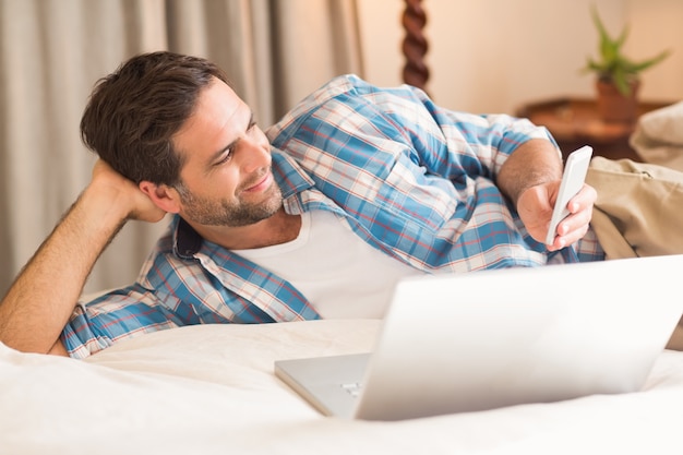 Handsome man relaxing on his bed with laptop