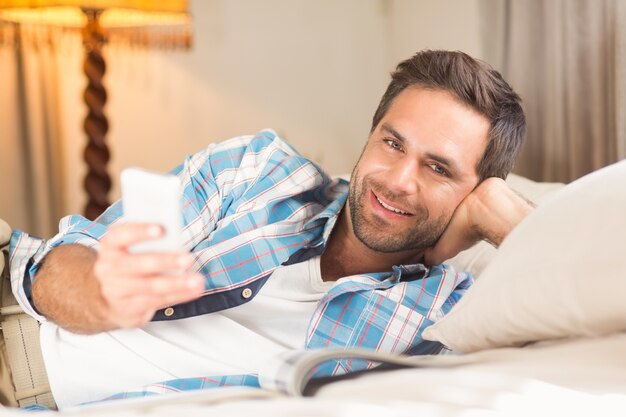Foto bell'uomo rilassante sul suo letto con il telefono