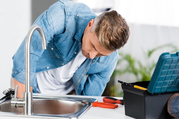 Handsome man repairing sink at kitchen