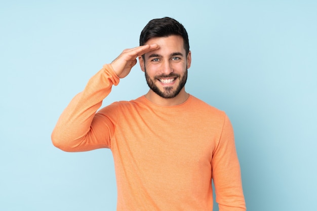 handsome man saluting with hand with happy expression over isolated blue