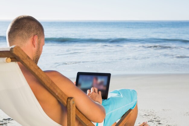 Handsome man scrolling on his tablet pc while sunbathing