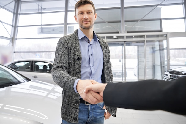 Handsome man shaking hand to female dealer in auto salon