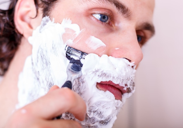 バスルームでひげを剃ってハンサムな男