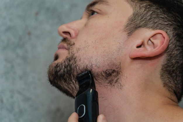 Handsome man shaving his beard by electric razor