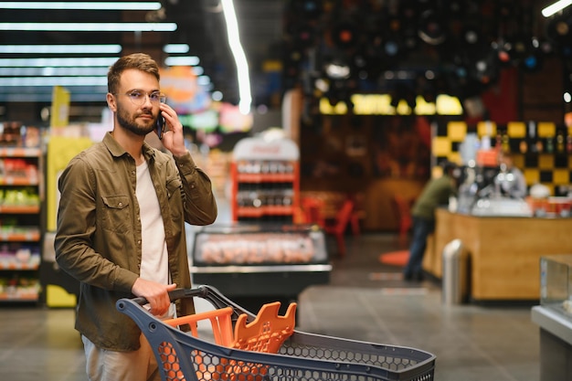 Handsome man shopping in supermarket smilling using phone