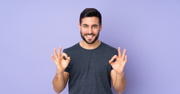 handsome man showing ok sign with two hands over isolated purple background