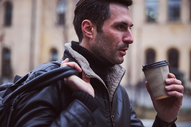 Handsome man sipping hot drink and walking outdoors