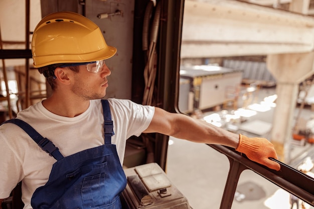 Handsome man sitting in operator cabin of industrial crane