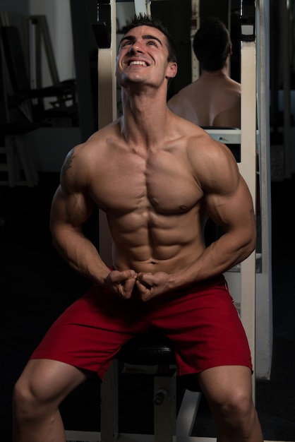 Handsome Man Sitting Strong In The Gym And Flexing Muscles  Muscular Athletic Bodybuilder Fitness Model Posing After Exercises