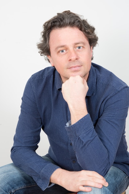 Handsome man sitting touching his chin while wearing blue shirt