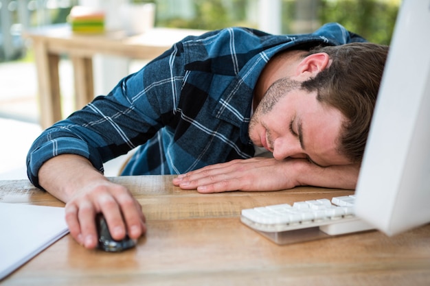 Uomo bello che dorme sul computer in un ufficio luminoso