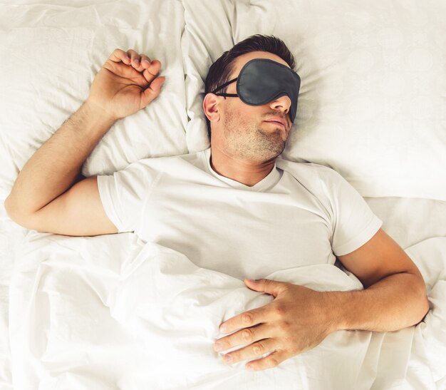 handsome man in sleeping mask in his bed