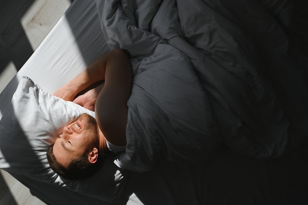 Photo handsome man sleeping under soft blanket in bed at home