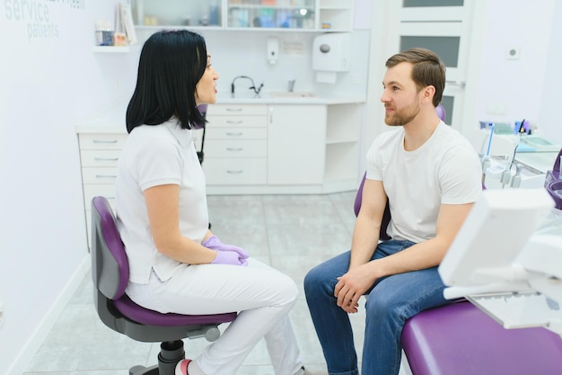 Bell'uomo sorridente durante l'esame dei denti paziente maschio felice seduto sulla sedia di un dentista e che controlla i denti