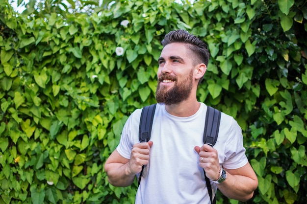 handsome man smiling, with his adventure backpack on a background of green and natural leaves.