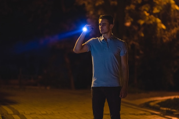 The handsome man stand with a flashlight on the dark street. night time