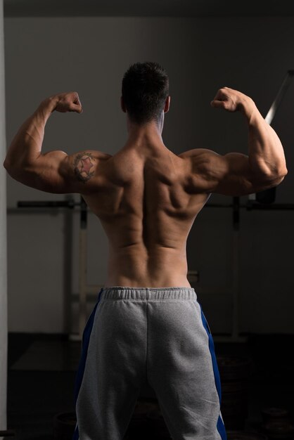 Bell'uomo in piedi forte in palestra e flettendo i muscoli modello di fitness bodybuilder atletico muscolare in posa dopo gli esercizi