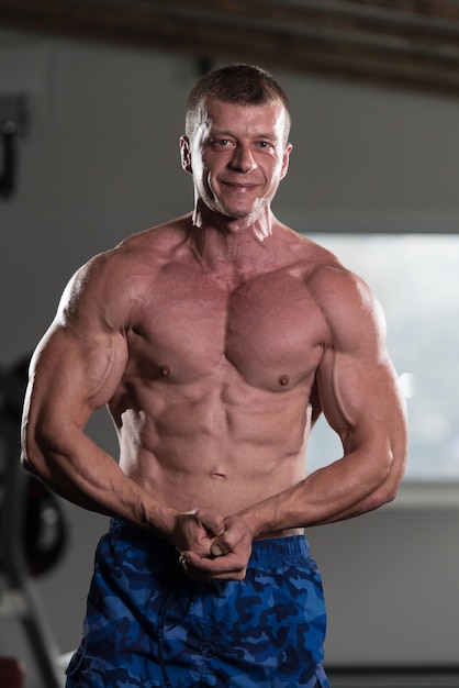 Handsome Man Standing Strong In The Gym And Flexing Muscles  Muscular Athletic Bodybuilder Fitness Model Posing After Exercises