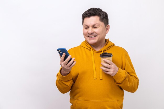 Handsome man standing with coffee and chatting on the phone expressing positive emotions