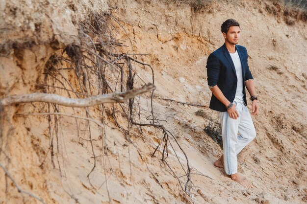 Handsome man in stylish clothes stands on sand background Place for text or advertising