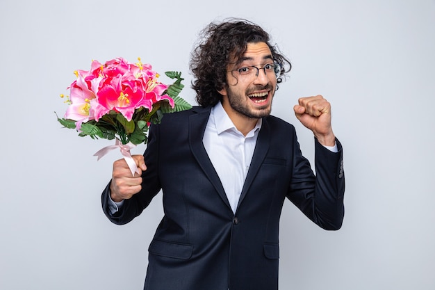 Handsome man in suit with bouquet of flowers looking happy and excited clenching fist