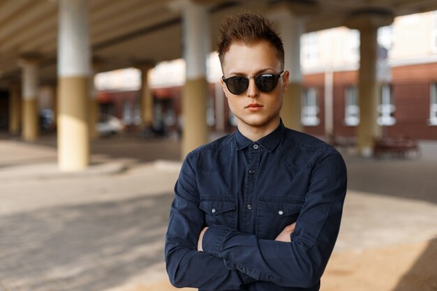 Handsome man in sunglasses and a fashionable shirt posing on the street on a sunny day