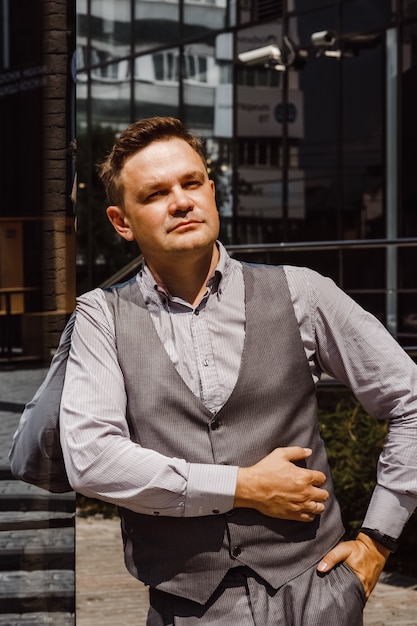 Handsome man in sunlight. Man on cityscape and buildings with reflections of city. Businessman in vest.