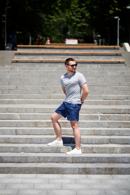 A handsome man in a T-shirt and shorts stands on the steps. Guy in sunglasses