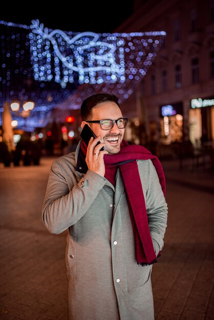 Handsome man talking on smartphone while walking on the street with Christmas decoration.