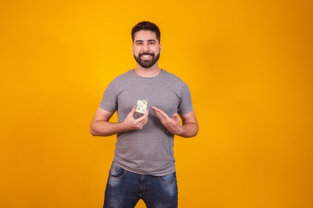 Handsome man tasting a piece of gorgonzola cheese on yellow background