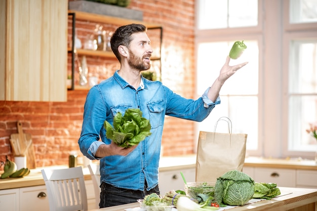 Handsome man throwing up green pepper while cooking vegan meals on the kitchen at home