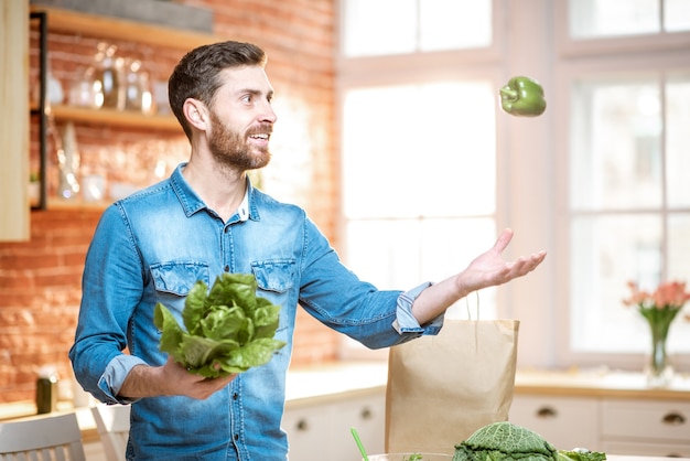 Handsome man throwing up green pepper while cooking vegan meals on the kitchen at home