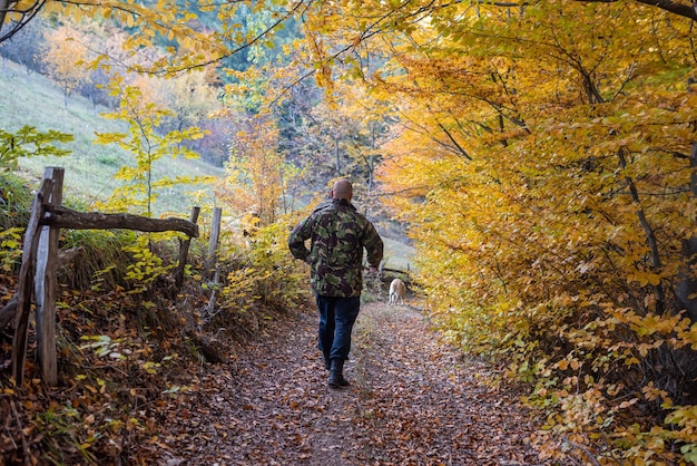 Photo a handsome man trail walking with his a dog in the autumn forest