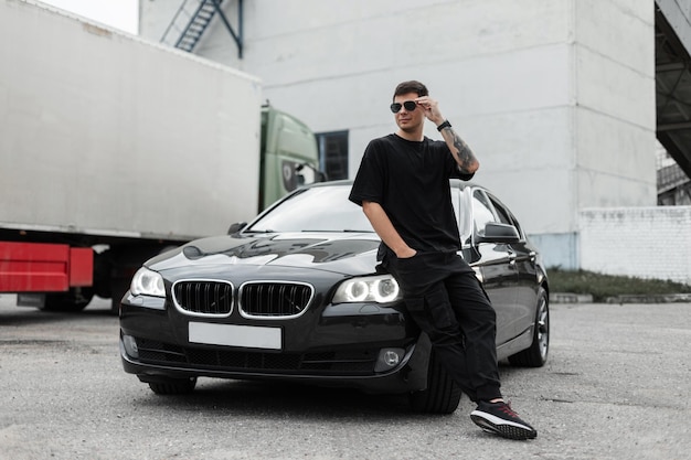 Foto un bell'uomo con una maglietta si trova vicino a un'auto nera acquisto e noleggio di un'auto