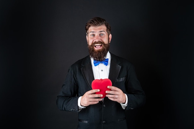 Handsome man in tuxedo holding love gift of heart for valentines day valentine