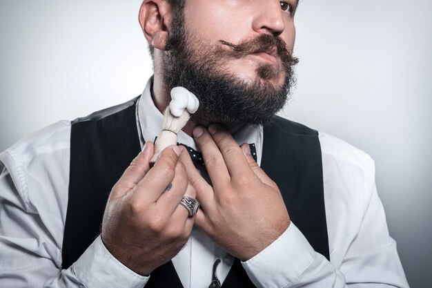 красивый мужчина использует щетку и пеногель для бритья бороды