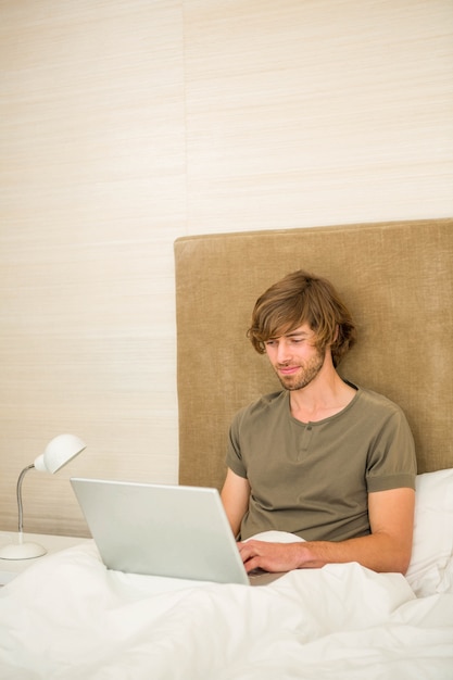 Handsome man using laptop in bed