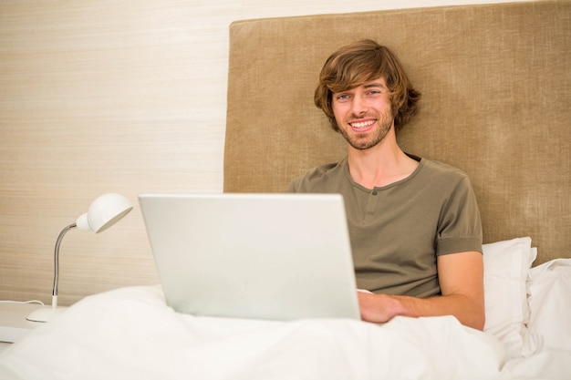 Handsome man using laptop in bed