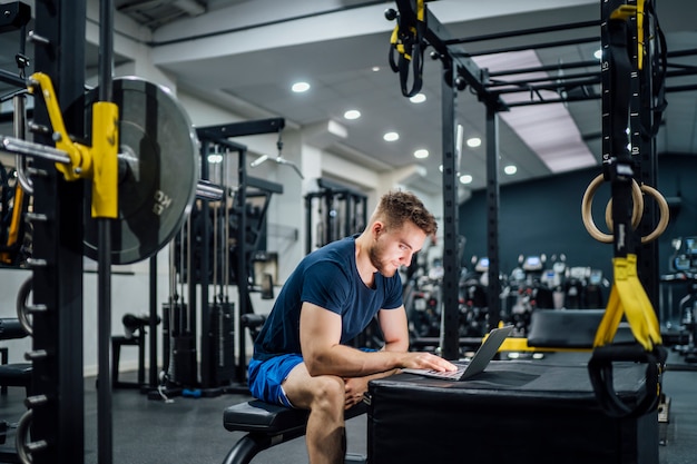 Uomo bello che utilizza computer portatile nella palestra