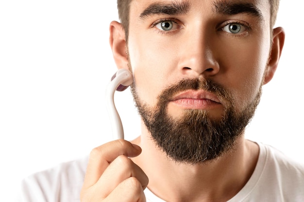 Handsome man using meso roller for better beard growth on white background